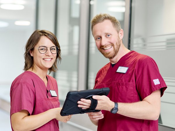 Zwei Pflegefachkräfte mit Tablet in der Hand im Stationsflur