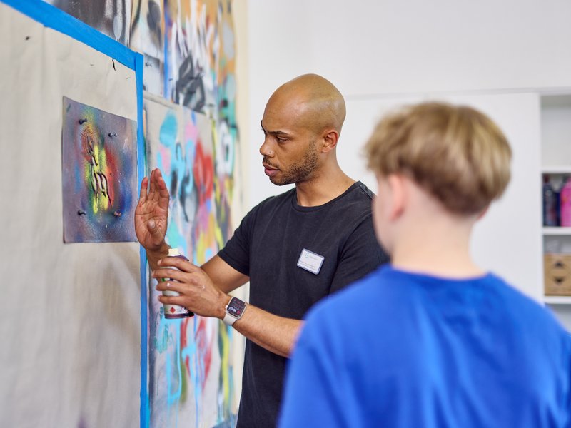 Kunsttherapeut erklärt einem jungen Patienten eine Maltechnik an der Wand