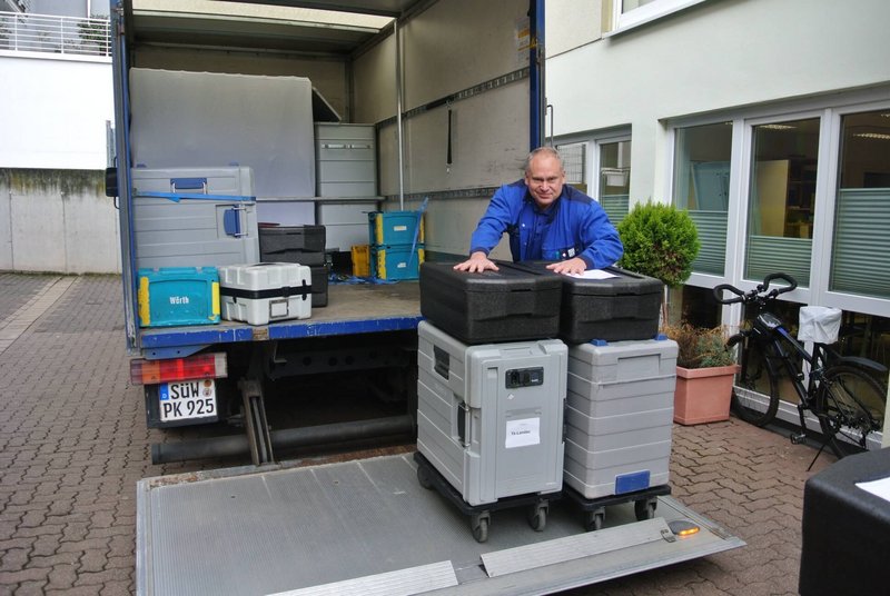 Ein Mitarbeiter in Arbeitskleidung belädt einen kleinen Lkw mit Kisten und Arbeitscontainern