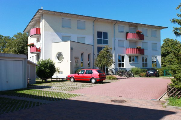 Blick auf einen Parkplatz mit einem parkenden Auto und ein helles Gebäude mit roten Balkonen