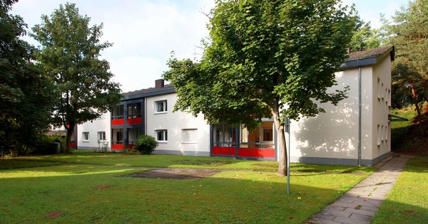 Blick auf ein Haus in Dahn mit Balkonen und Terrassen, davor eine grüne Wiese mit Bäumen