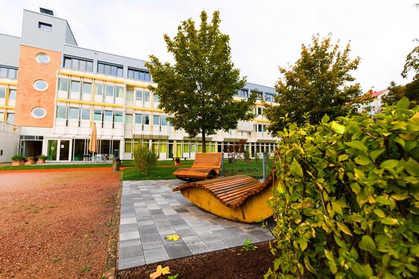 Blick auf zwei Liegen und einen Baum vor dem Klinikgebäude in Kaiserslautern