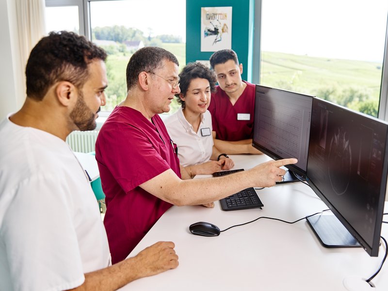 Chefarzt erklärt einem Ärzt*innenteam etwas am Computer