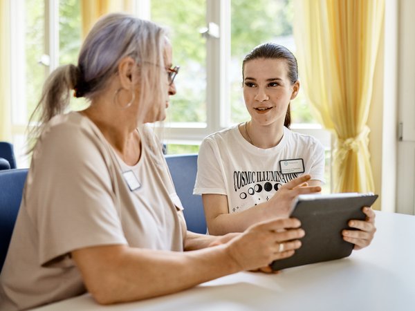 Praxisanleiterin und Schülerin sitzen an einem Tisch und besprechen etwas auf einem Tablet