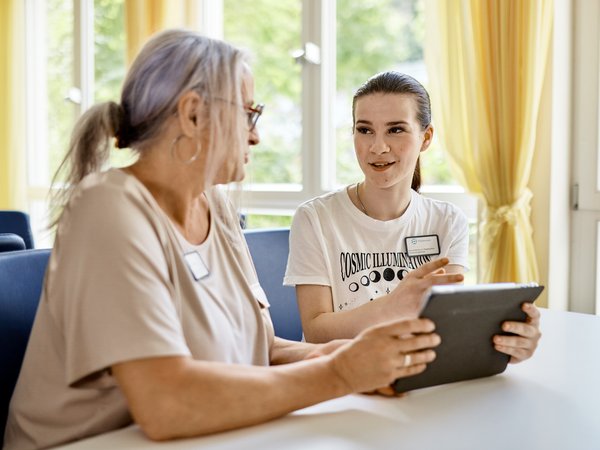 Praxisanleiterin sitzt mit Schülerin am Tisch und erklärt etwas am Tablet