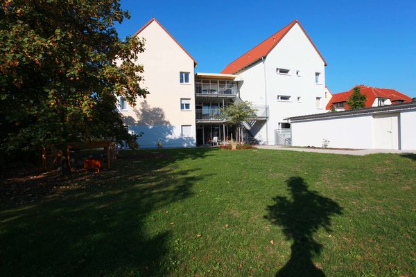 Blick auf ein weißes Haus mit rotem Dach in Maikammer, davor eine grüne Wiese