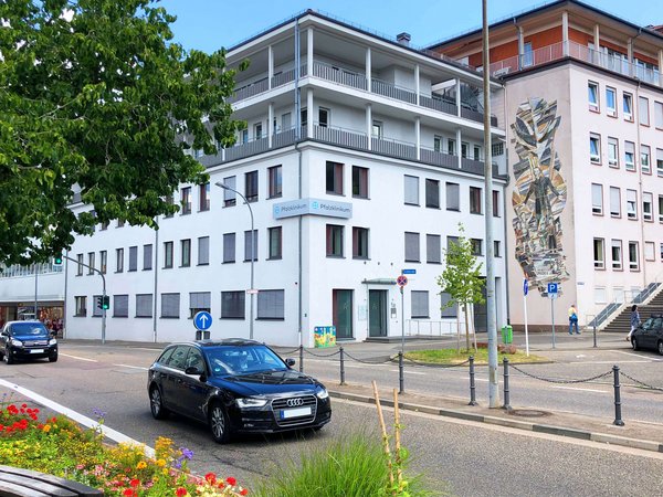 Blick auf eine Straße mit Autos und das weiße Gebäude der Tagesklinik in Pirmasens