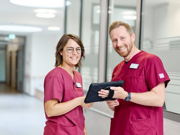 Zwei Pflegekräfte stehen im Stationsflur und haben Tablet dabei