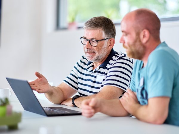 Zwei Personen sitzen an einem Laptop und reden